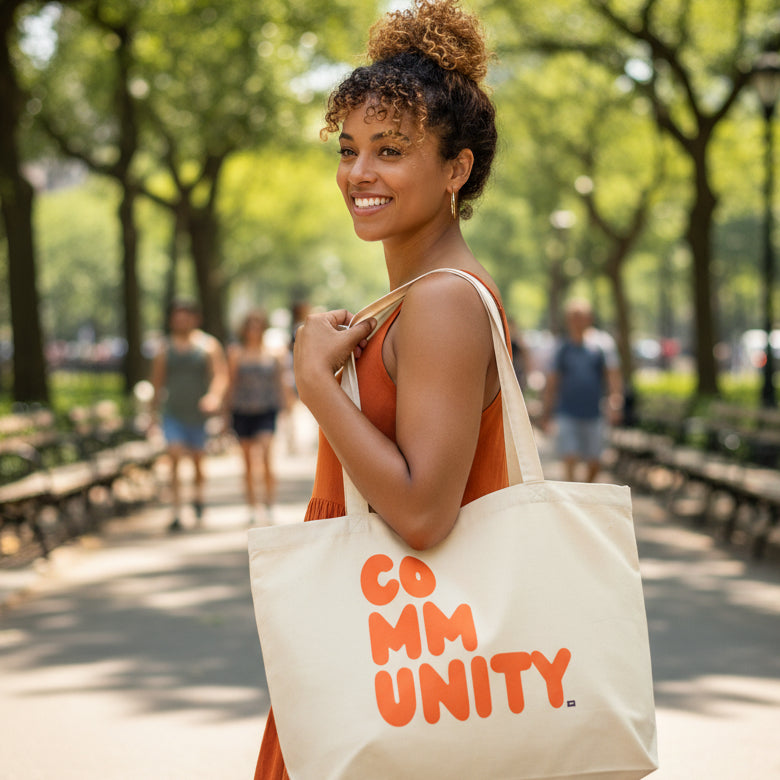 Woman carrying the APWT Gift Shop's A Community in Orange Citrus Jumbo Tote Bag from the Community Collection in Natural 