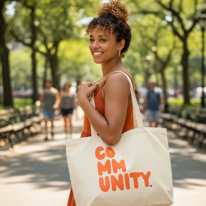 Woman carrying the APWT Gift Shop's A Community in Orange Citrus Jumbo Tote Bag from the Community Collection in Natural 