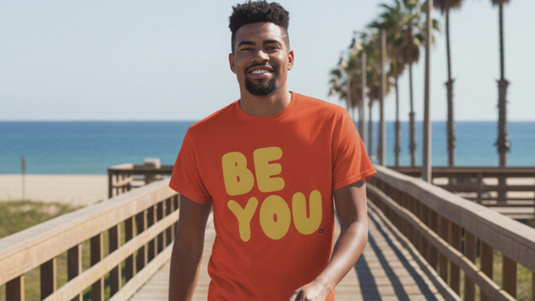 Man at the beach wearing the APWT Gift Shop's Be You in Orange and Yellow Unisex T-Shirt from the Be You Collection