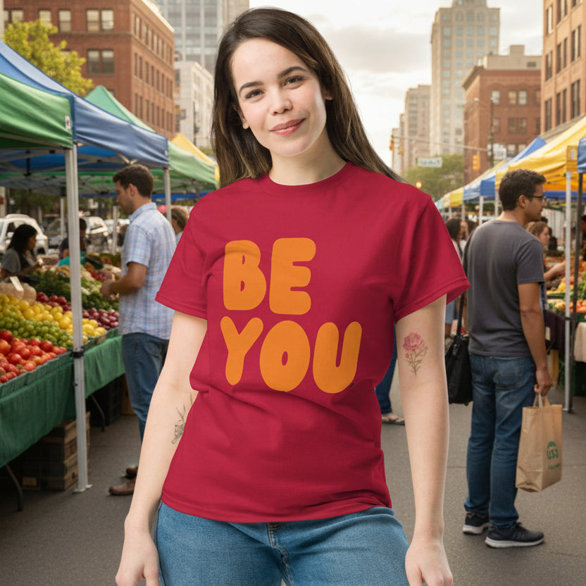 Woman at a farmer's market wearing the APWT Gift Shop's Be You in Apple Red and Orange Unisex T-Shirt from the Be You Collection