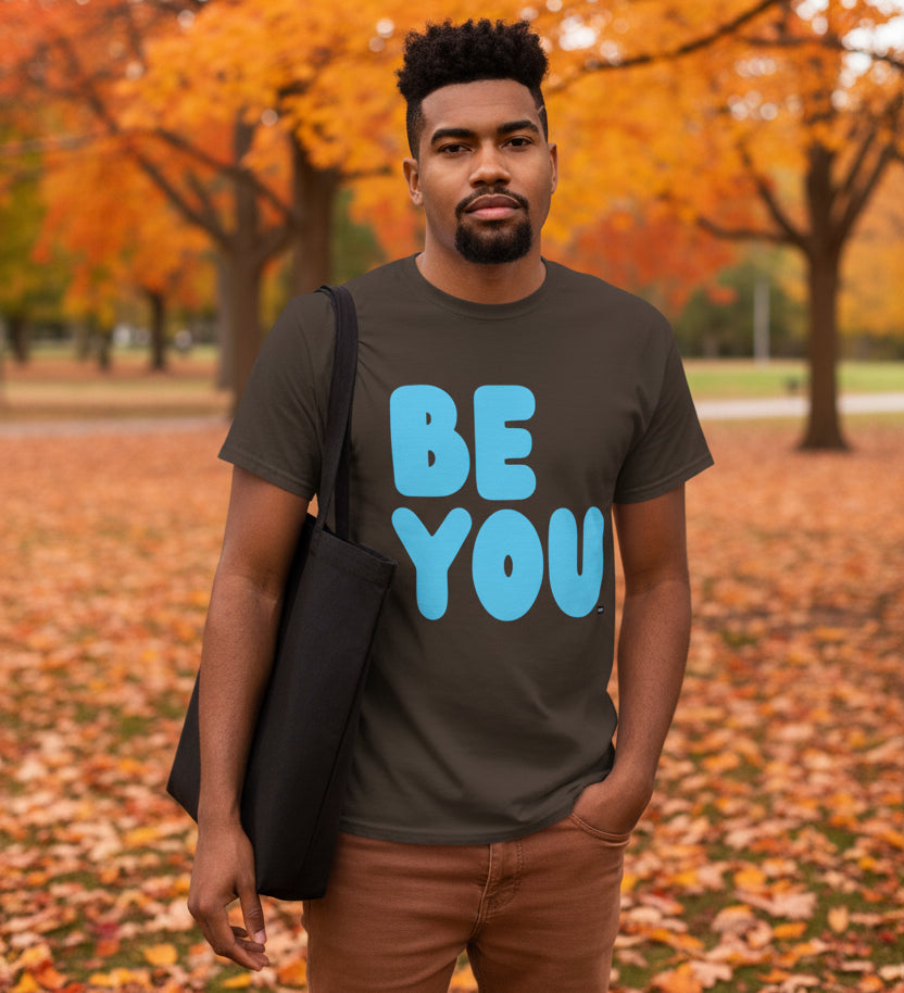 Man standing in the park on an autumn day wearing the APWT Gift Shop's Be You in Brown and Blue Unisex T-Shirt from the Be You Collection