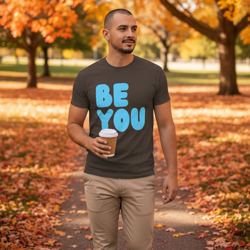 Man walking through the park on an autumn day wearing the APWT Gift Shop's Be You in Brown and Blue Unisex T-Shirt from the Be You Collection
