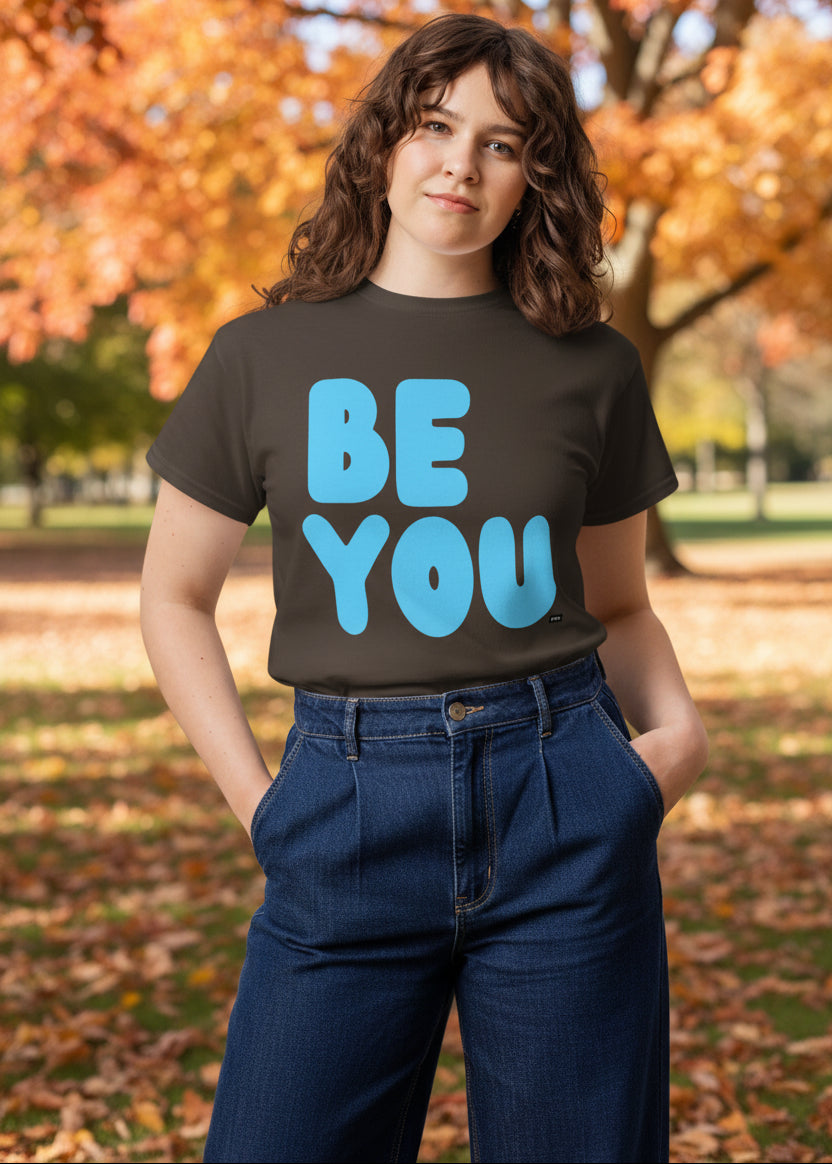 Woman standing in the park on an autumn day wearing the APWT Gift Shop's Be You in Brown and Blue Unisex T-Shirt from the Be You Collection