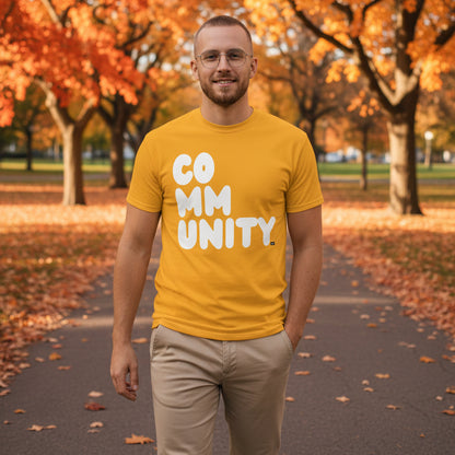 Man standing in the park on an autumn day wearing the APWT Gift Shop's A Community in Sunflower Yellow Unisex T-Shirt from the Community Collection