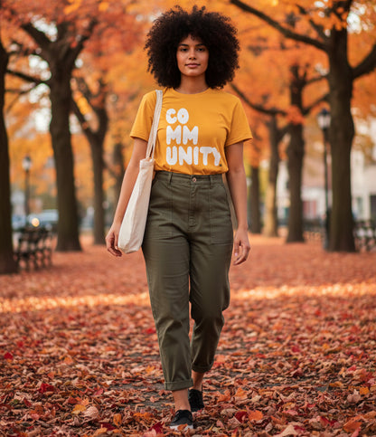 Woman walking through the park on an autumn day wearing the APWT Gift Shop's A Community in Sunflower Yellow Unisex T-Shirt from the Community Collection