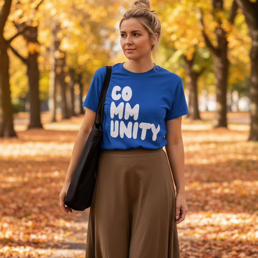 Woman walking through the park on an autumn day wearing the APWT Gift Shop's A Community in Ocean Blue Unisex T-shirt from the Community Collection