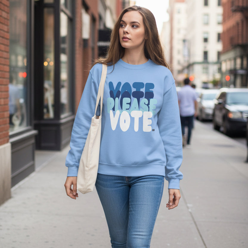 Woman walking down a city street wearing the APWT Gift Shop's Please Vote in Sky Blue Unisex Crew Neck Sweatshirt from the APWT Vote Shop