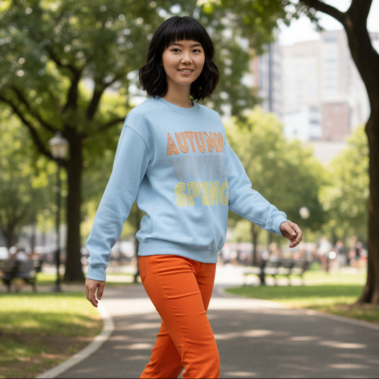 Woman walking through the park wearing the APWT Gift Shop's Fall in Autumn Unisex Crew Neck Sweatshirt from the Day in the Life Collection in Light Blue