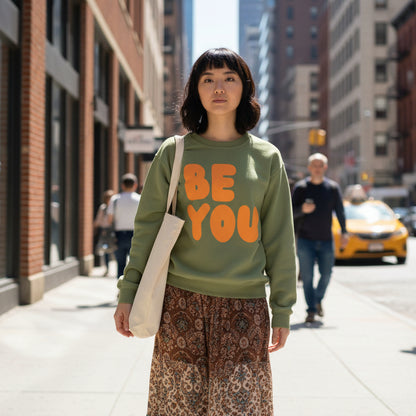 Woman walking down the street wearing The APWT Gift Shop's Be You in Olive Green and Orange Unisex Crew Neck Sweatshirt from the Be You Collection 