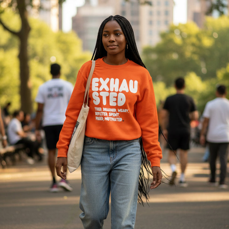 Woman walking through a city park wearing the APWT Gift Shop's Exhausted in Orange Unisex Crew Neck Sweatshirt from the Exhausted Collection