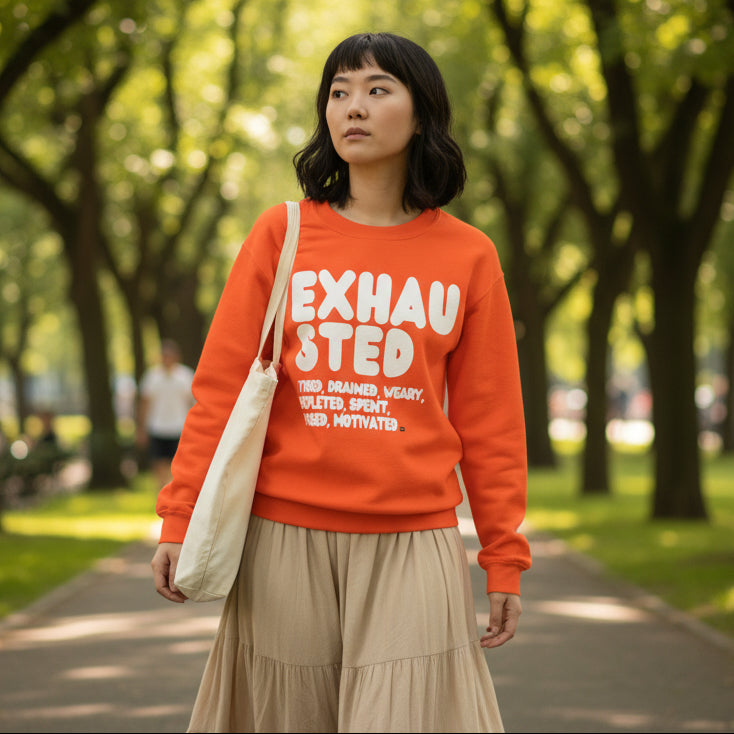 Woman walking through a city park wearing the APWT Gift Shop's Exhausted in Orange Unisex Crew Neck Sweatshirt from the Exhausted Collection