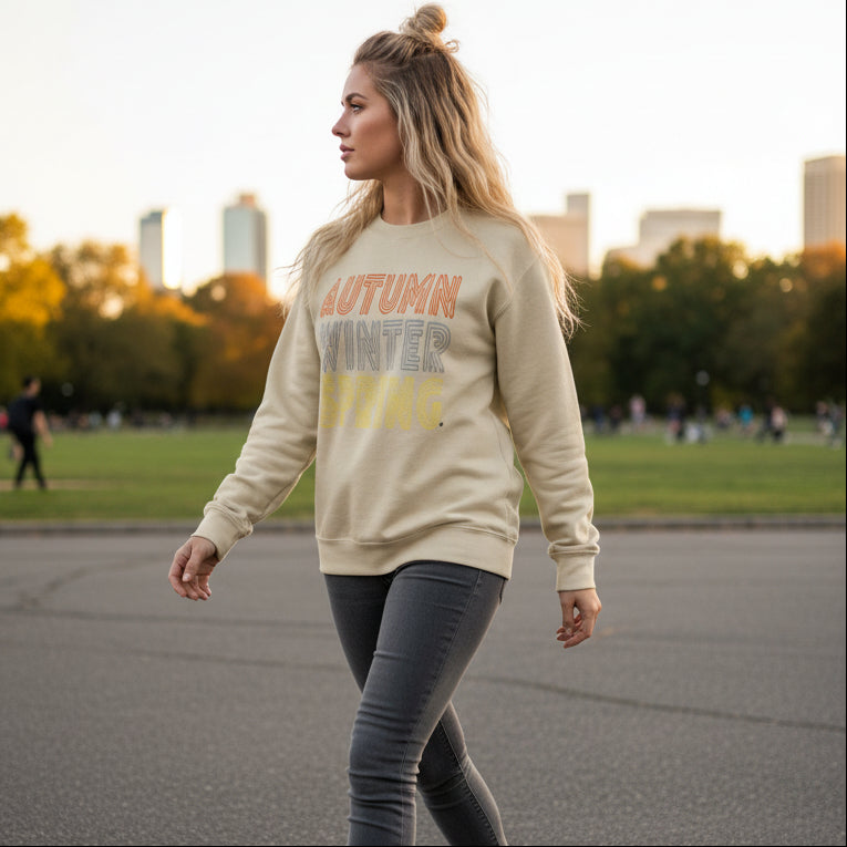 Woman walking through the park wearing the APWT Gift Shop's Fall in Autumn Unisex Crew Neck Sweatshirt from the Day in the Life Collection in Beige