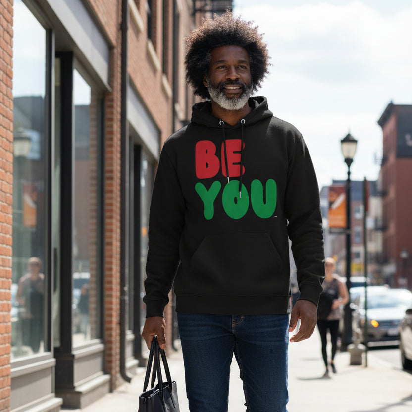 Man walking down the street wearing the APWT Gift Shop's Be You in Black Premium Unisex Hoodie from the Black Collection and Premium Basics Collection