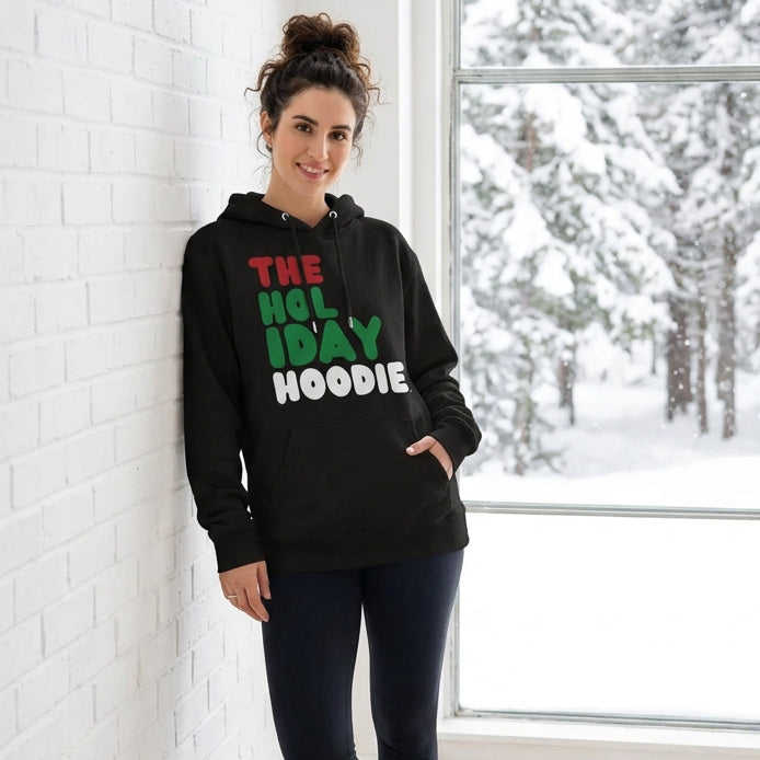 Woman standing in a white room wearing The Holiday Hoodie Premium Unisex Hoodie from the APWT Holiday Shop and the Day in the Life Collection in Black
