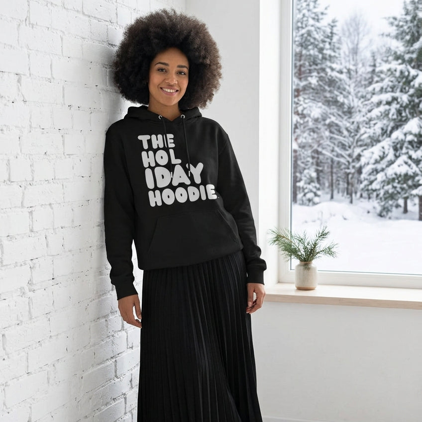 Woman standing in a white room wearing The APWT Gift Shop's The Holiday Celebration Premium Unisex Hoodie from the APWT Holiday Shop and the Day in the Life Collection