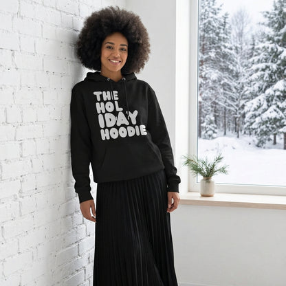Woman standing in a white room wearing The APWT Gift Shop's The Holiday Celebration Premium Unisex Hoodie from the APWT Holiday Shop and the Day in the Life Collection