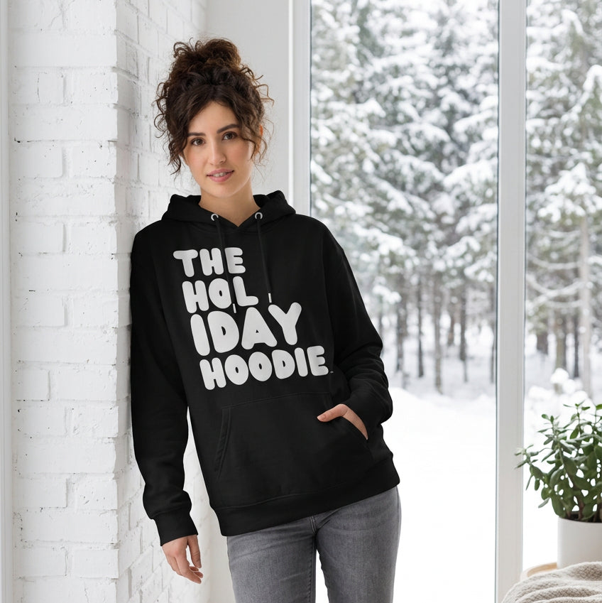 Woman standing in a white room wearing The APWT Gift Shop's The Holiday Celebration Premium Unisex Hoodie from the APWT Holiday Shop and the Day in the Life Collection