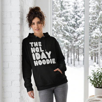 Woman standing in a white room wearing The APWT Gift Shop's The Holiday Celebration Premium Unisex Hoodie from the APWT Holiday Shop and the Day in the Life Collection