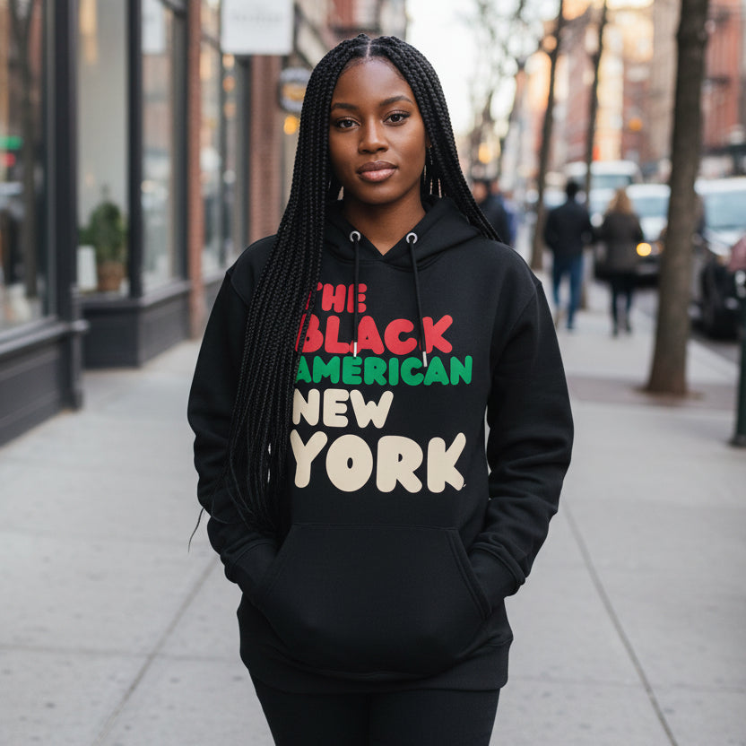 Woman standing on a city street wearing the APWT Gift Shop's The Black American New York Premium Unisex Hoodie from the Black Collection and the Premium Basics Collection