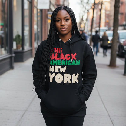 Woman standing on a city street wearing the APWT Gift Shop's The Black American New York Premium Unisex Hoodie from the Black Collection and the Premium Basics Collection