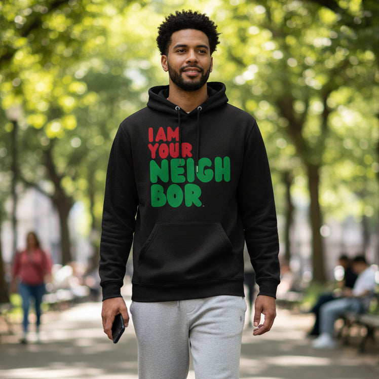 Man walking through a city park wearing the APWT Gift Shop's I Am Your Neighbor in Black Premium Unisex Hoodie from the Black Collection and the  Premium Basics Collection