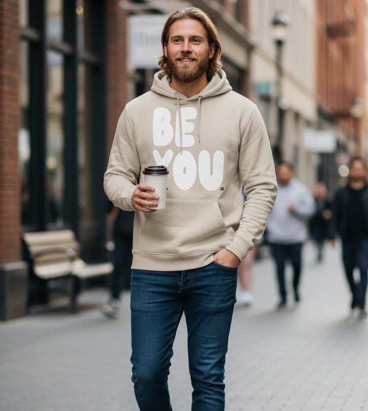 Man walking down a city street wearing the APWT Gift Shop's Be You in Beige and White Premium Unisex Hoodie from the Be You Collection and the Premium Basics Collection