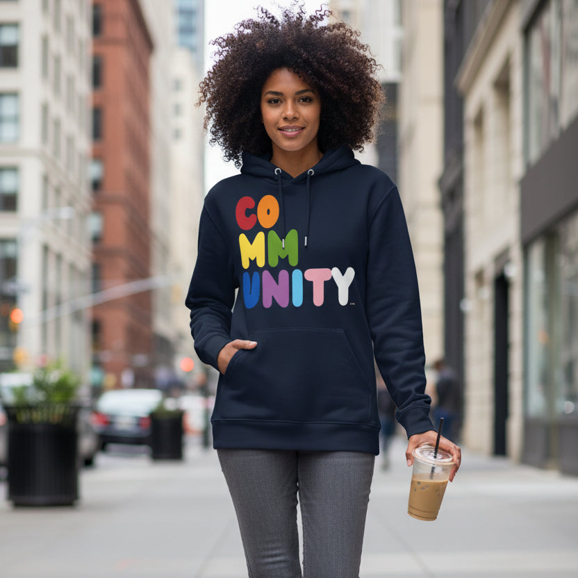 Woman walking down a city sidewalk wearing the APWT Gift Shop's Rainbow Community Premium Unisex Hoodie from the Community Collection and the Pride in the APWT Gift Shop Collection