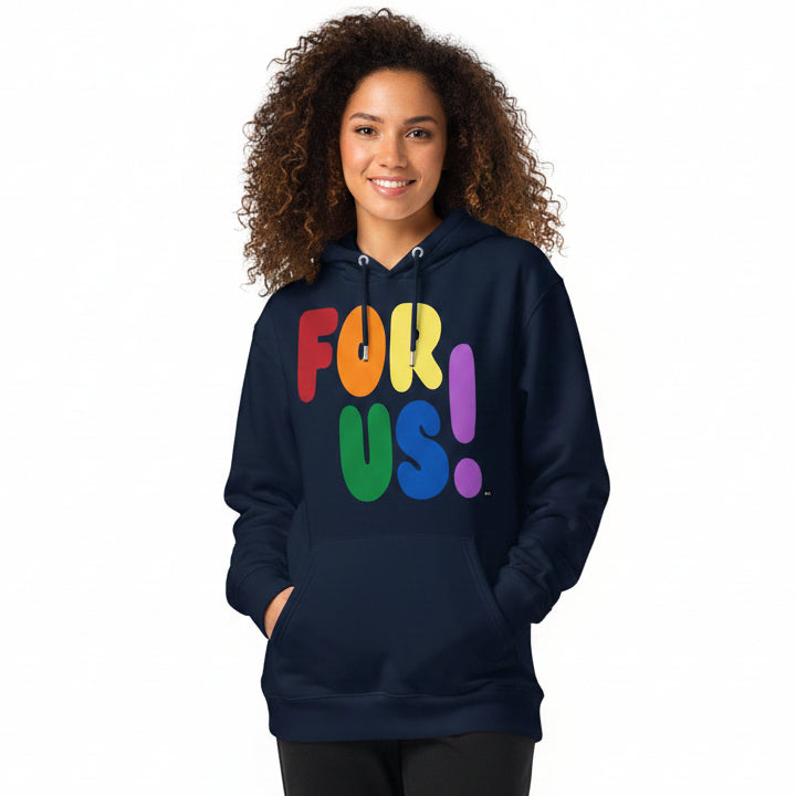 Woman wearing the APWT Gift Shop's Rainbow For Us Premium Unisex Hoodie featuring the 'For Us' message in the colors of the LGBTQ+ Pride Flag