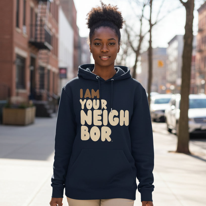 Woman walking down a city street wearing the APWT Gift Shop's I Am Your Neighbor Premium Unisex Hoodie from the Day in the Life Collection and the Premium Basics Collection in Navy Blue