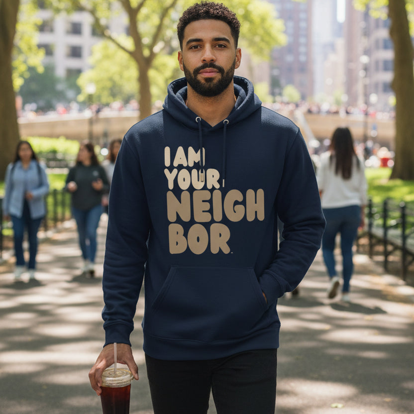 man walking through a city park wearing the APWT Gift Shop's I Am Your Neighbor in Brown Premium Unisex Hoodie from the Day in the Life Collection and the Premium Basics Collection in Navy Blue