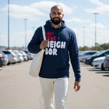 Man walking through a parking lot wearing the APWT Gift Shop's I Am Your Neighbor in Turmoil Premium Unisex Hoodie from the Day in the Life Collection and the Premium Basics Collection