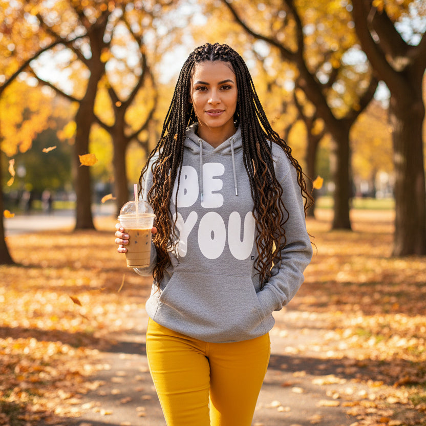 Woman walking through a city park on an autumn day wearing the APWT Gift Shop's Be You in Grey and White Premium Unisex Hoodie from the Be You Collection