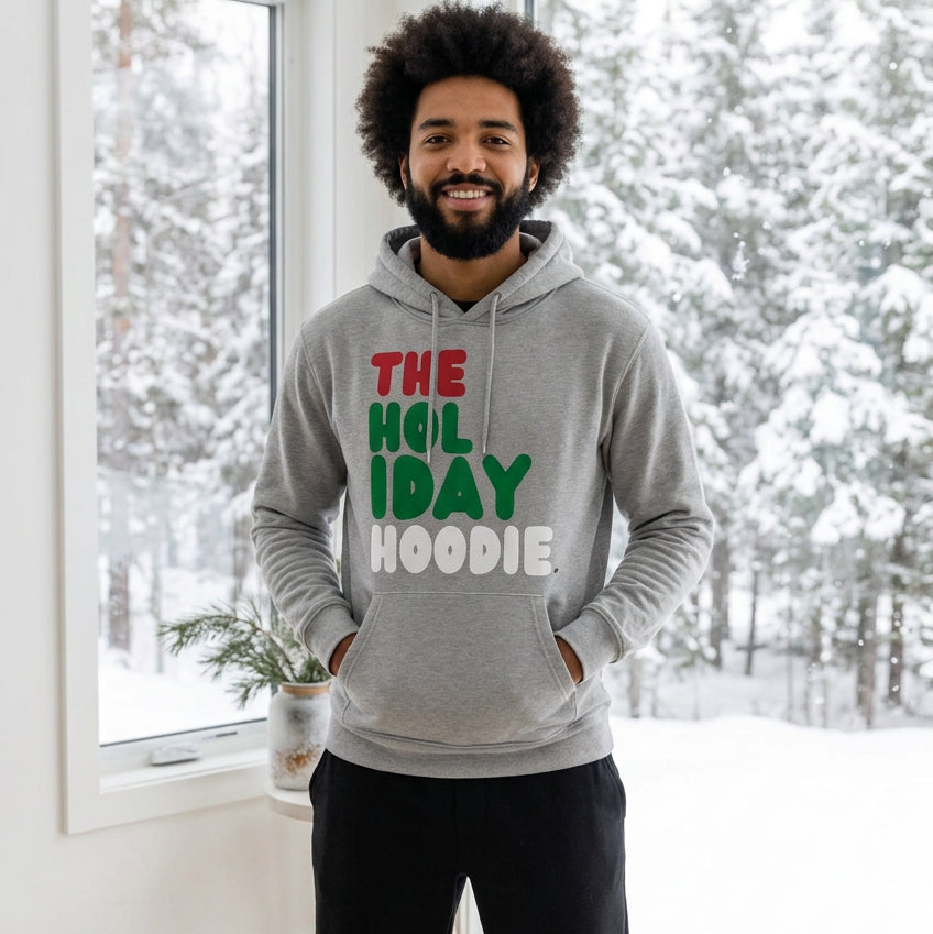Man standing in a white room wearing The Holiday Hoodie Premium Unisex Hoodie from the APWT Holiday Shop and the Day in the Life Collection in Grey