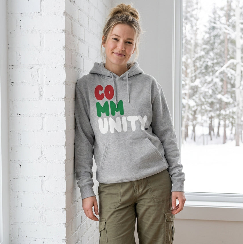 Woman standing in a white room wearing The APWT Gift Shop's Holiday Community Premium Unisex Hoodie from the Community Collection and the APWT Holiday Shop