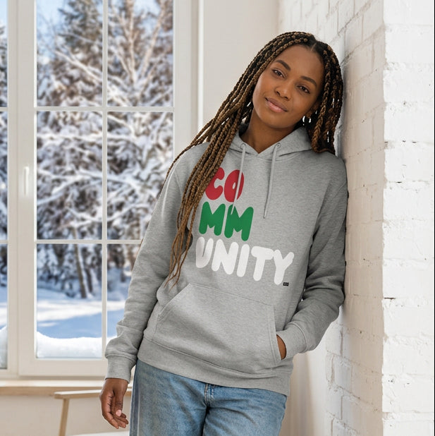 Woman standing in a white room wearing The APWT Gift Shop's Holiday Community Premium Unisex Hoodie from the Community Collection and the APWT Holiday Shop