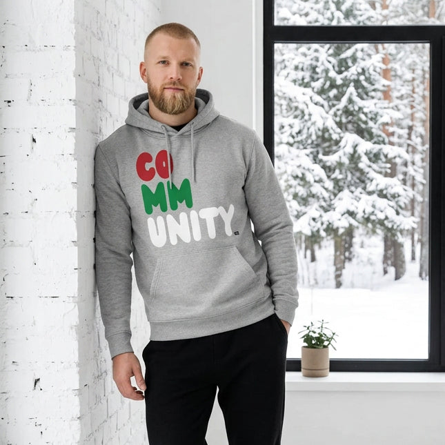 Man standing in a white room wearing The APWT Gift Shop's Holiday Community Premium Unisex Hoodie from the Community Collection and the APWT Holiday Shop