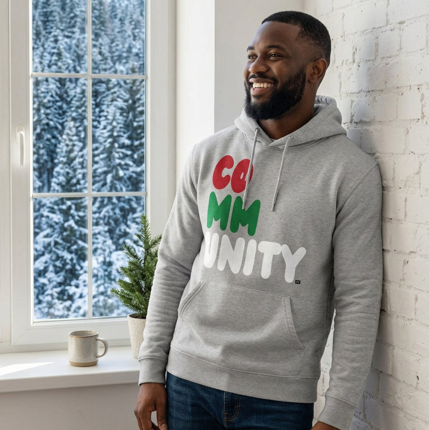Man standing in a white room wearing The APWT Gift Shop's Holiday Community Premium Unisex Hoodie from the Community Collection and the APWT Holiday Shop