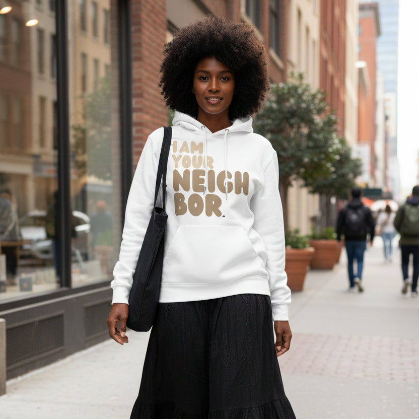 Woman walking down a city street wearing the APWT Gift Shop's I Am Your Neighbor in Brown Premium Unisex Hoodie from the Day in the Life Collection and the Premium Basics Collection in White