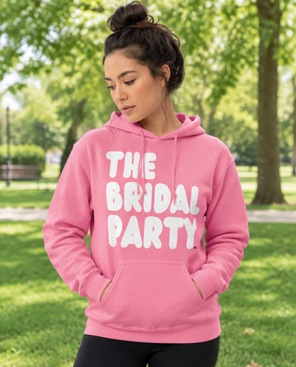 Woman standing in a park wearing the APWT Gift Shop's The Bridal Party Unisex Hoodie from the APWT Wedding Shop in Pink