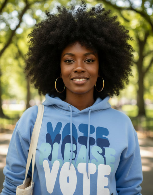 Woman walking through a city park wearing the APWT Gift Shop's Please Vote in Sky Blue Unisex Hoodie from the APWT Vote Shop