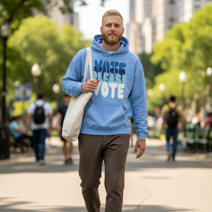 Man walking through a city park wearing the APWT Gift Shop's Please Vote in Sky Blue Unisex Hoodie from the APWT Vote Shop