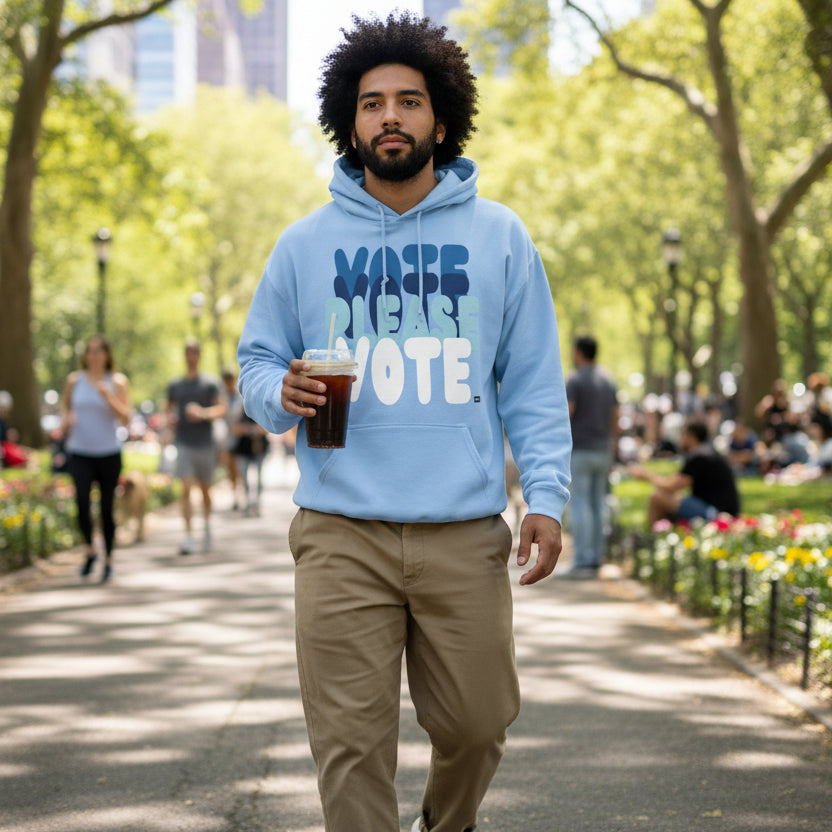 Man walking through a city park wearing the APWT Gift Shop's Please Vote in Sky Blue Unisex Hoodie from the APWT Vote Shop