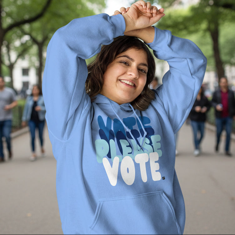 Woman in city park wearing Please Vote in Sky Blue Unisex Hoodie from the APWT Gift Shop -  Vote Advocacy Sweatshirt