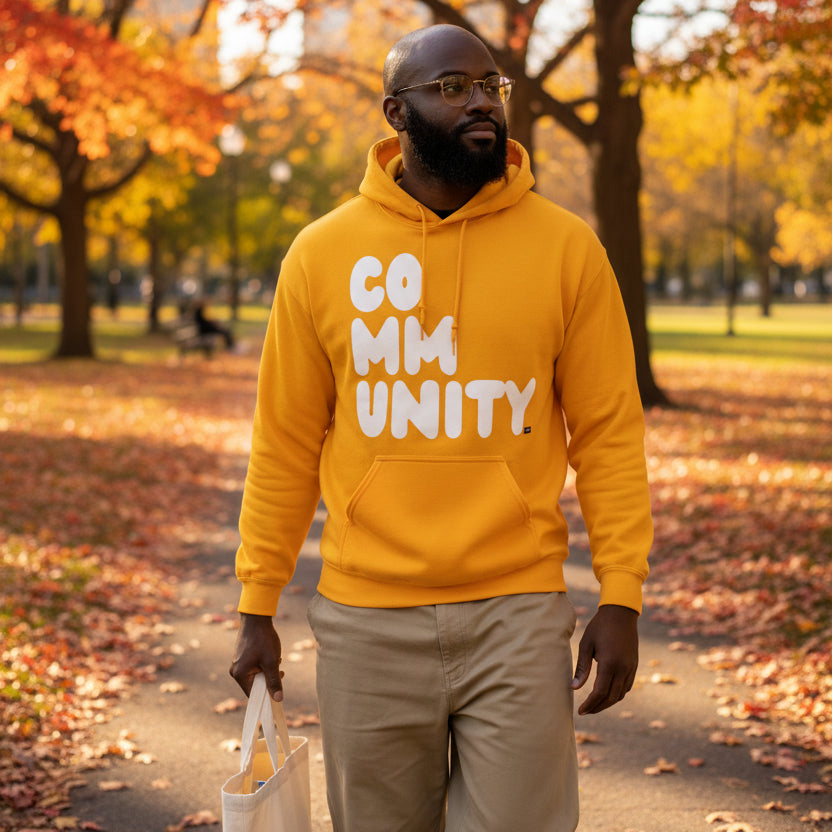Man walking through a city park wearing the APWT Gift Shop's A Community in Sunny Yellow Unisex Hoodie from the Community Collection