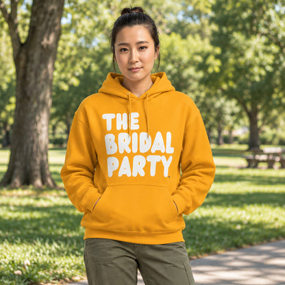 Woman standing in a park wearing the APWT Gift Shop's The Bridal Party Unisex Hoodie from the APWT Wedding Shop in Gold/Yellow