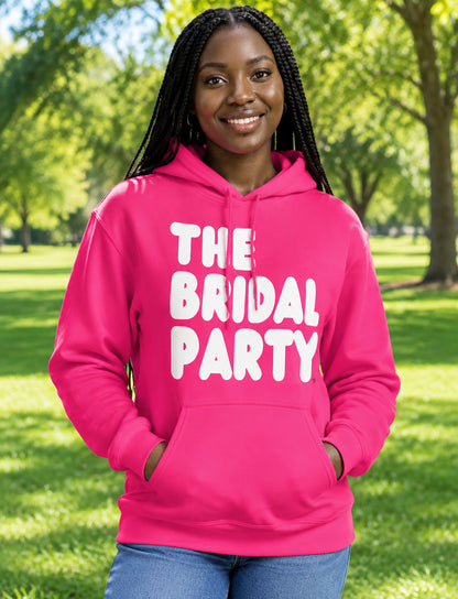 Woman standing in a park wearing the APWT Gift Shop's The Bridal Party Unisex Hoodie from the APWT Wedding Shop in Hot Pink