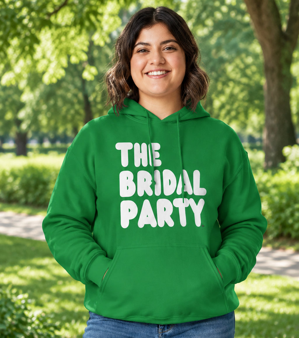 Woman standing in a park wearing the APWT Gift Shop's The Bridal Party Unisex Hoodie from the APWT Wedding Shop in Green