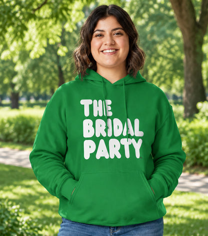 Woman standing in a park wearing the APWT Gift Shop's The Bridal Party Unisex Hoodie from the APWT Wedding Shop in Green