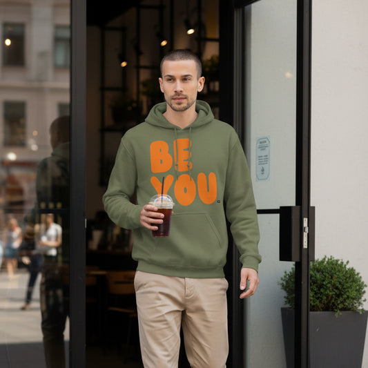 Man walking out of a coffee shop wearing the APWT Gift Shop's Be You in Olive Green and Orange Unisex Hoodie from the Be You Collection