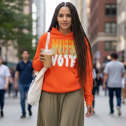 Woman walking down a city street wearing the APWT Gift Shop's Please Vote in Safety Cone Orange Unisex Hoodie from the APWT Vote Shop